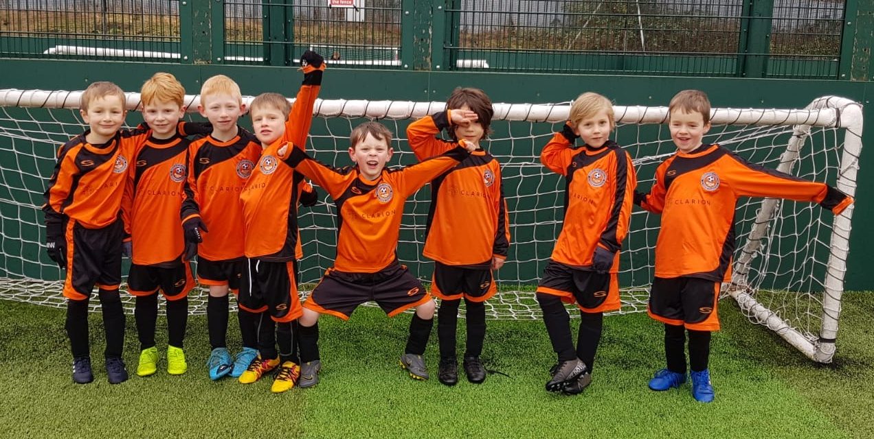 Under 7 Ashton on Mersey Football team standing in fromt of a football goal with orange and black kit on