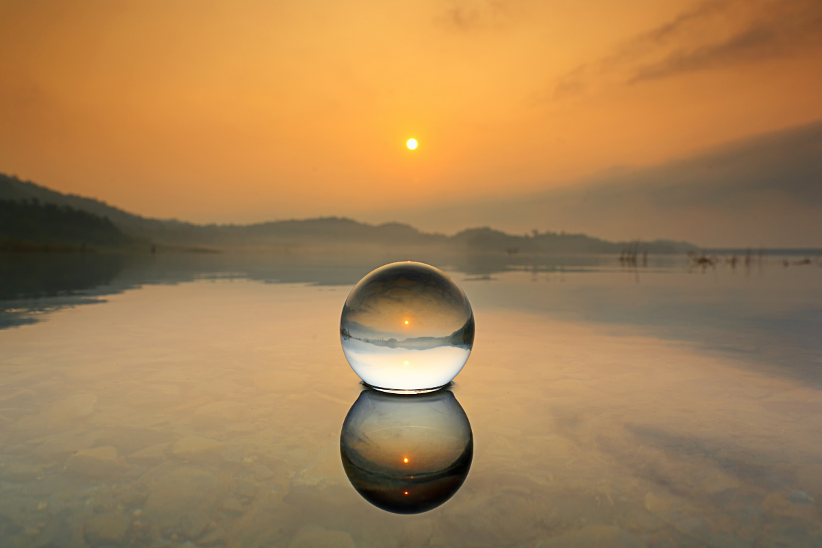 Stock market forecasts for 2023: Crystal ball in a desert setting with a sun setting over mountains behind it. The picture is intended to related to Keith Thompson's economic and stock market commentary about forecasting the future events over the next year.