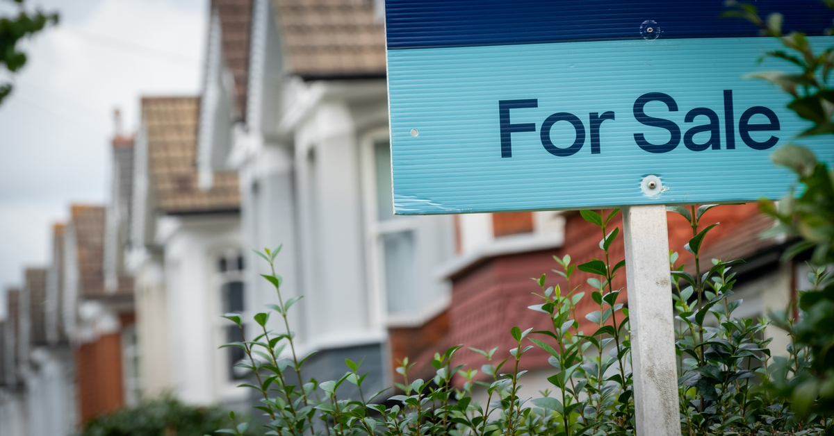 A “for sale” sign in front of a row of residential houses.