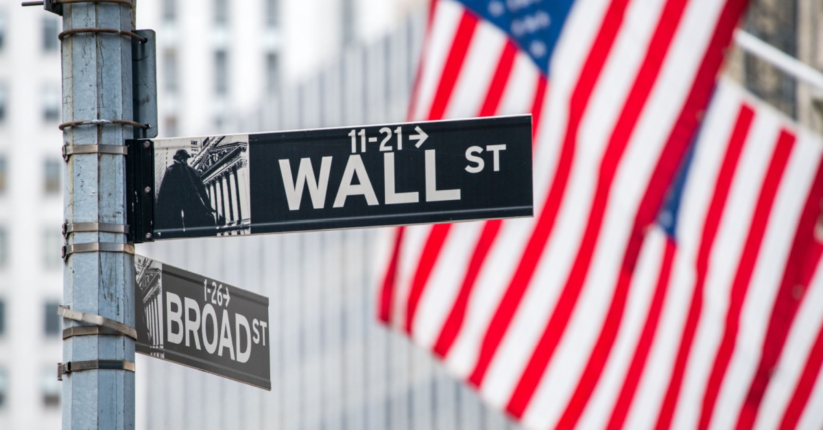 A “Wall St” street sign with American flags behind.