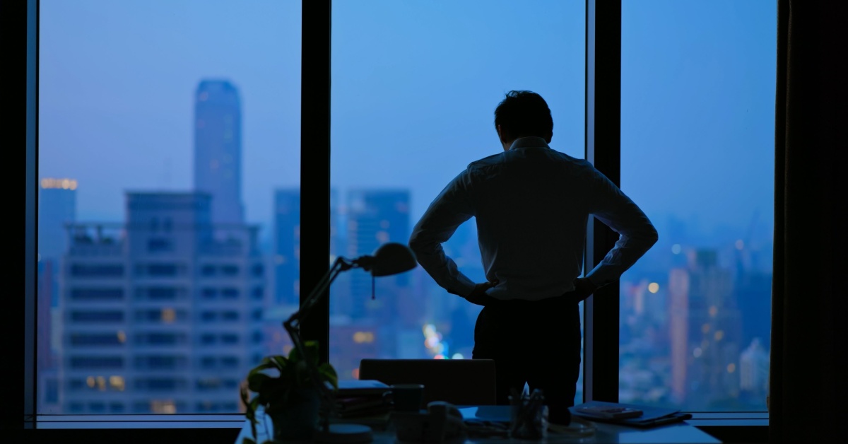 A solitary businessman looks out of a window.