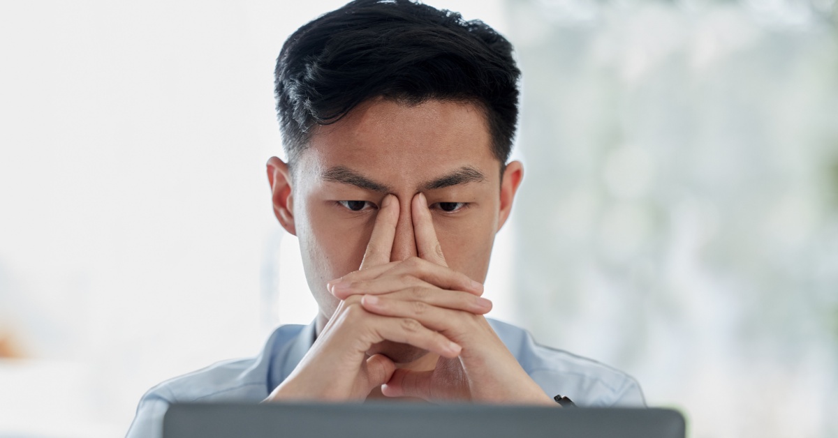 A man sitting at a laptop and pinching his eyes.