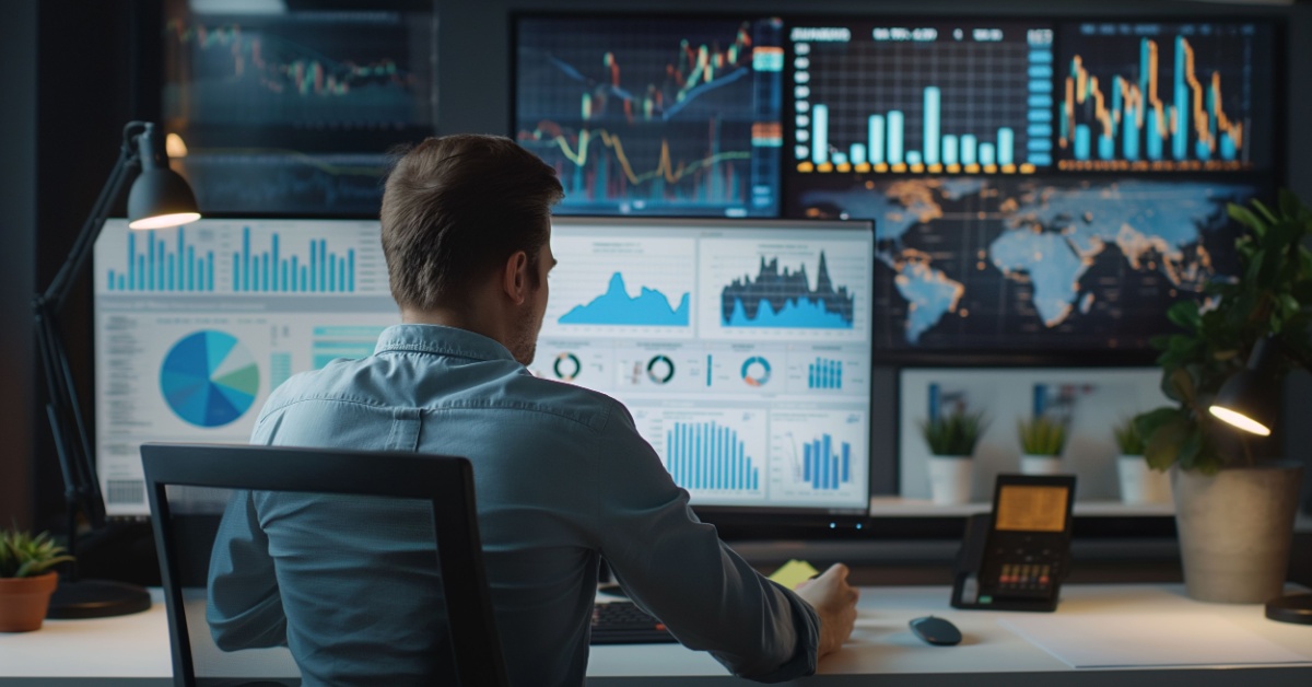 A man looking at multiple computer screens with different indices on them.