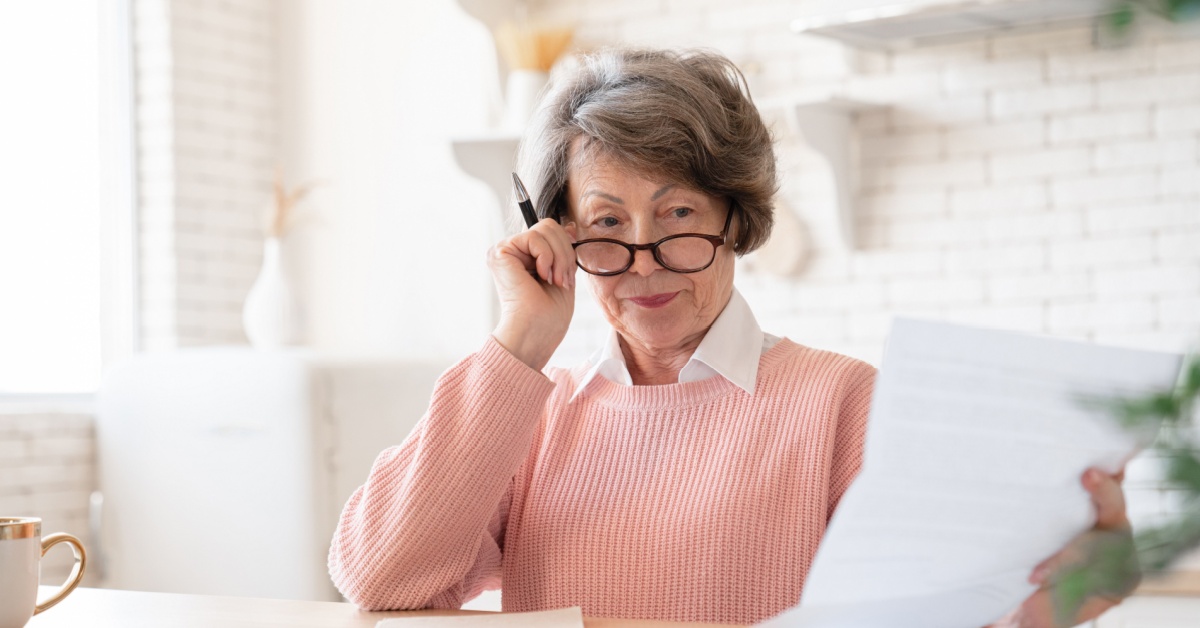 An older woman reading documents with a pen and calculator to hand