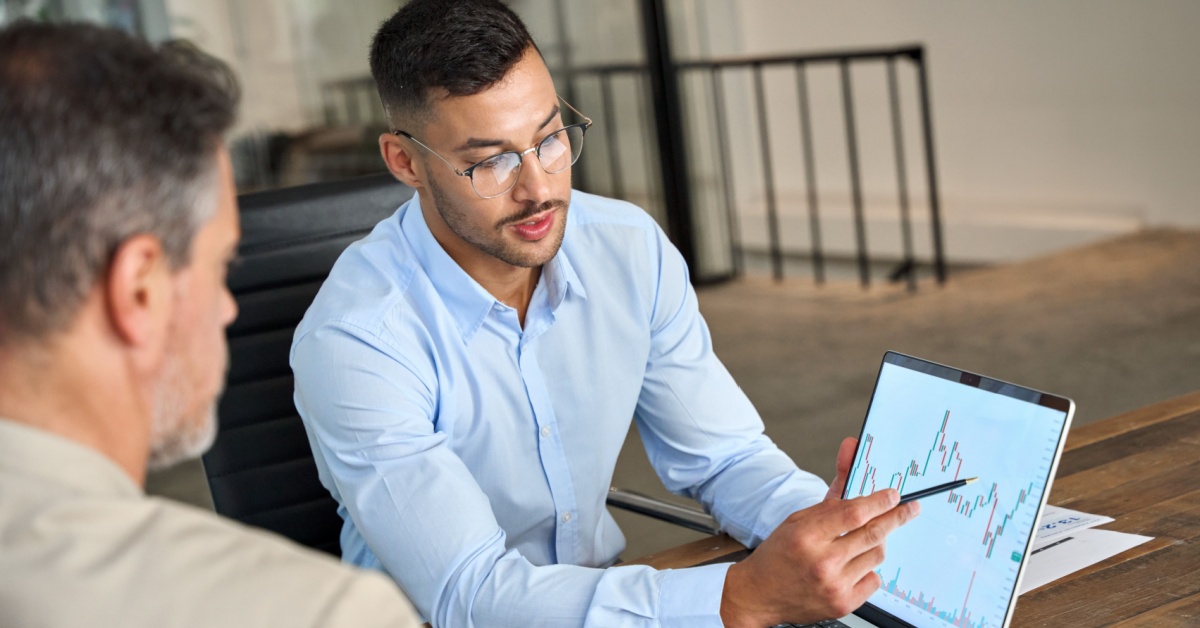 One man showing another market performance on a computer