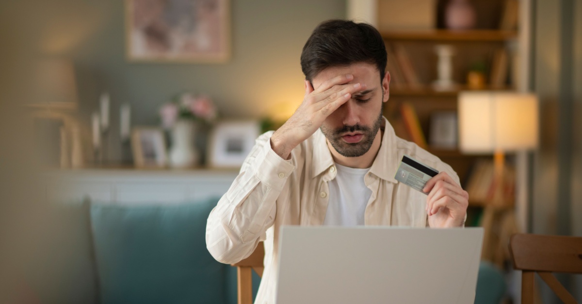 A concerned man holding a card and looking at a computer screen.