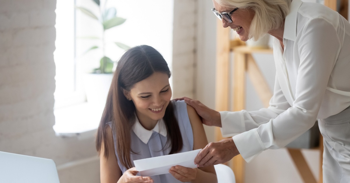 An older woman passing a younger woman an envelope